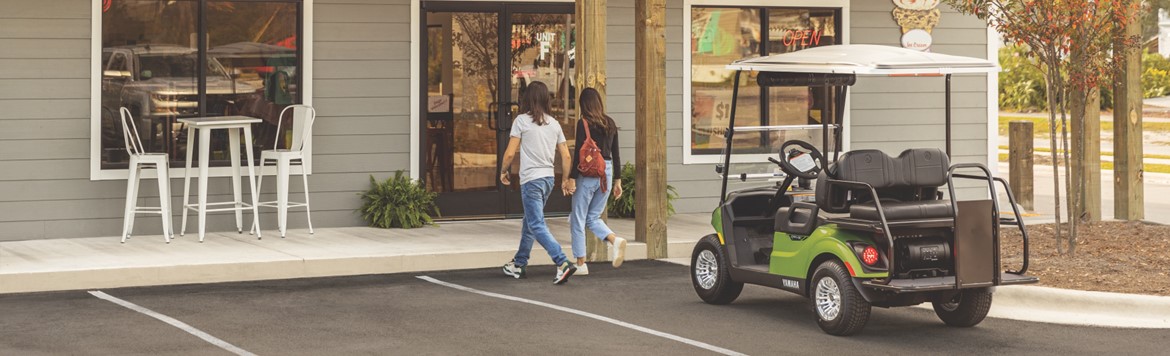 Young couple holding hands walking towards ice cream shop's entrance, after leaving their green …